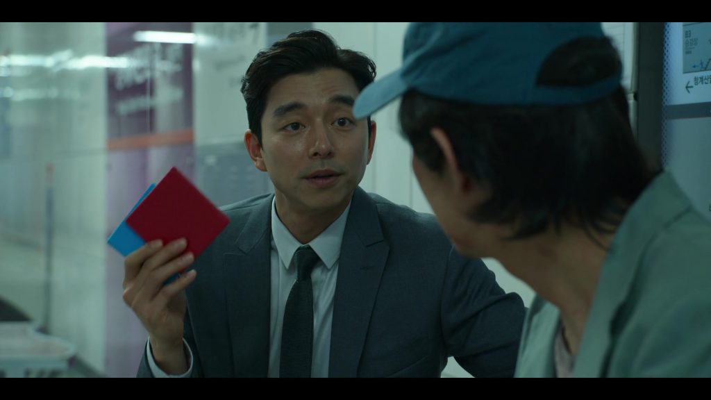 The Salesman’s Proposal: Red and Blue Envelopes in Squid Game Salesman offering Gi-hun a choice between red and blue envelopes in "Squid Game."