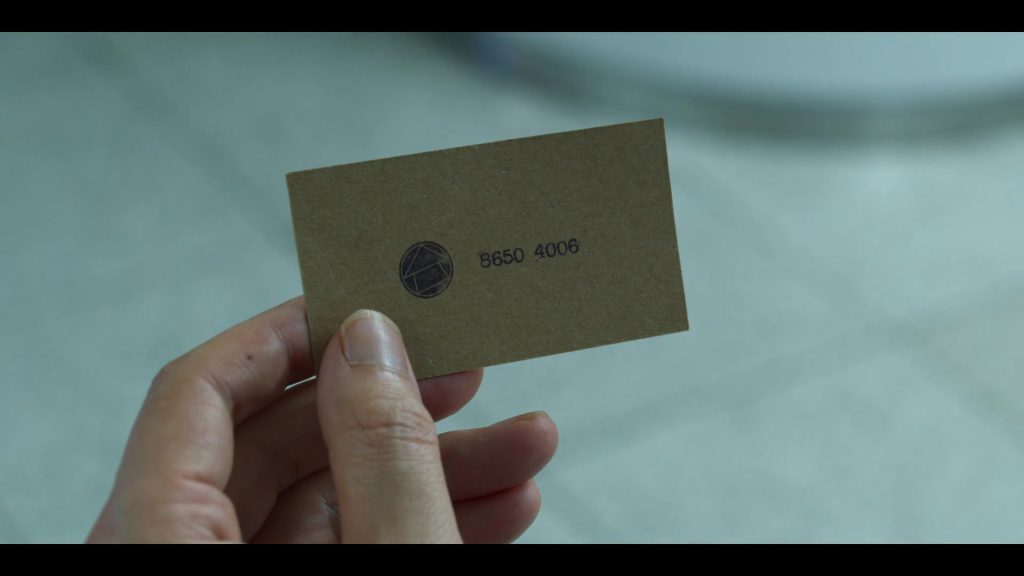 Close-Up of Squid Game Invitation Card with Cryptic Details Squid Game invitation card with a geometric design and number.