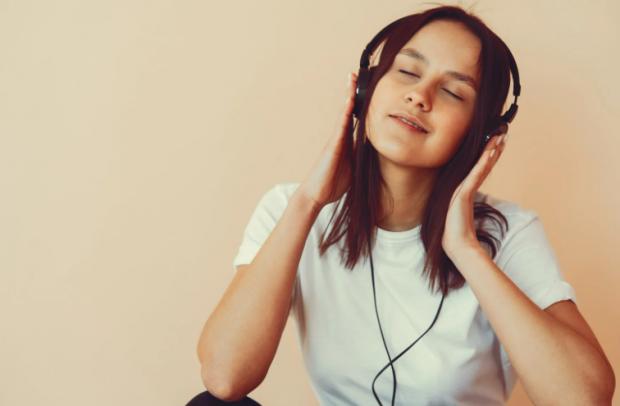 Smiling woman wearing headphones, immersed in a Spotify podcast for language learning.
