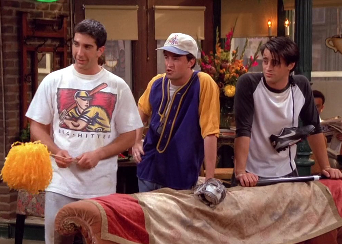 "Ross, Joey, and Chandler in softball outfits, standing in Central Perk."