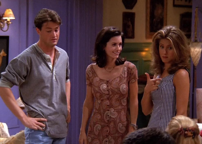 "Rachel gesturing playfully while standing next to Monica and Chandler in Friends Season 1 Episode 3."