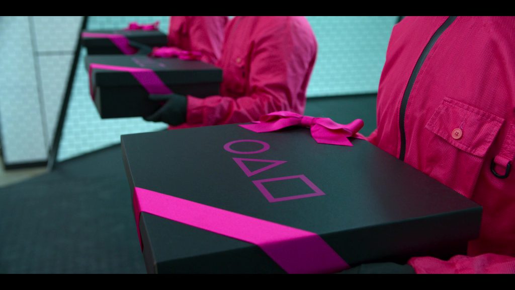 Gift box with pink ribbon and PlayStation symbols from Squid Game Episode 8.