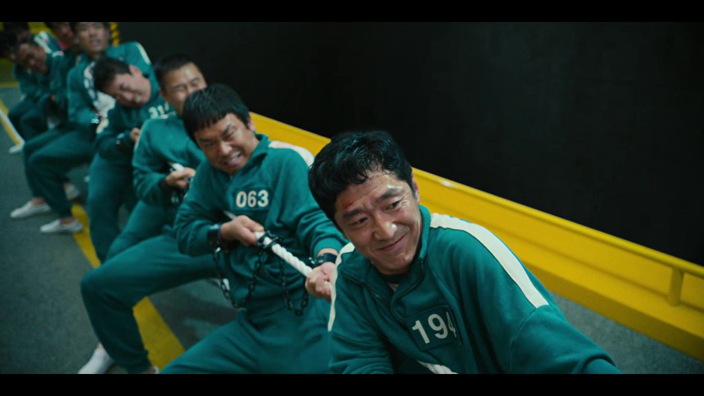 "Players in Squid Game participating in a high-stakes tug-of-war, useful for learning English action and strategy vocabulary."