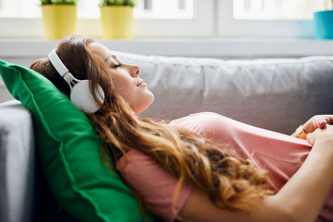 Woman enjoying a podcast on Spotify for language learning while relaxing on a couch.