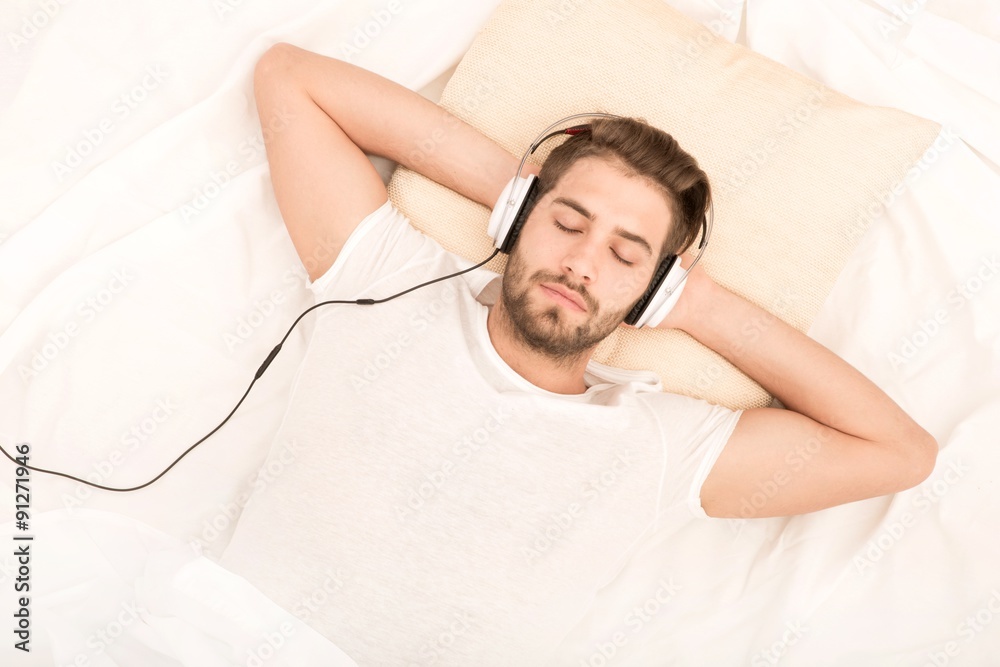 A man relaxing on a bed with headphones, enjoying language learning with Spotify.