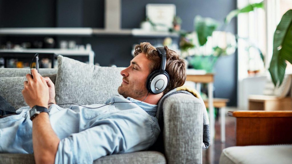 Man lying on a couch wearing headphones, practicing language learning with podcasts.