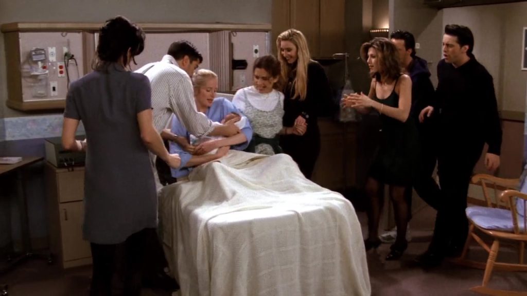 Carol surrounded by friends during childbirth in Friends S01E23, illustrating the concept of Movie For Language learning.