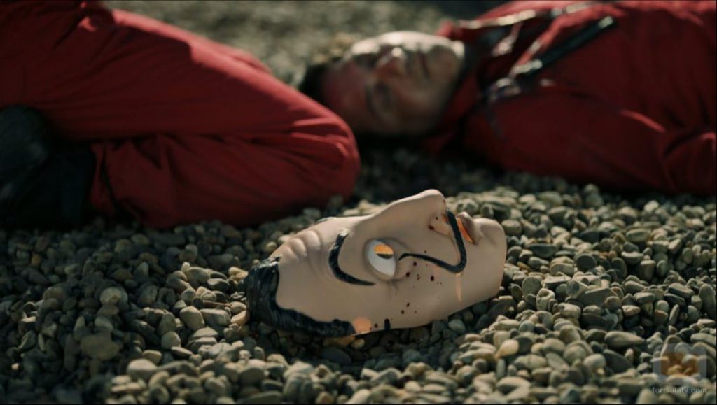 A bloody mask resting on gravel beside a person in a red suit, from a tense scene in “Monet Heist S01 E04.”