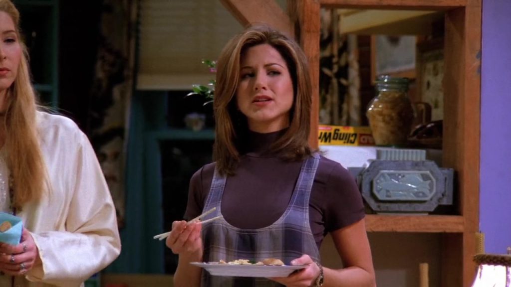 Rachel holding a plate of food with chopsticks in a scene from Friends S01E16.