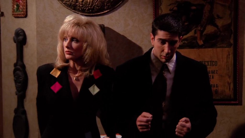 Ross and a blonde woman standing together at a bar scene in Friends.