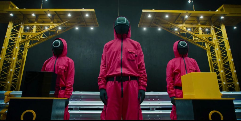 "Masked guards from Squid Game standing in red uniforms, perfect for learning vocabulary related to dystopia and control."