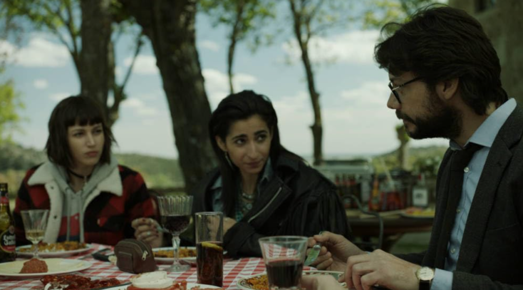 Characters from Money Heist sitting at an outdoor table, having a serious conversation over a meal.