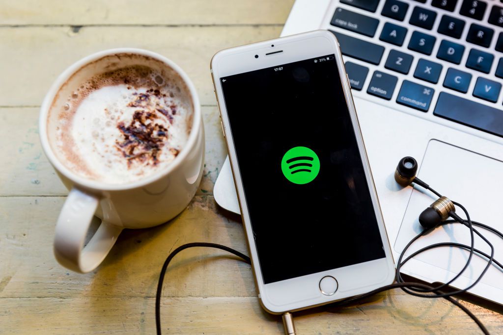 Smartphone showing the Spotify app next to a coffee cup and headphones, illustrating a language learning setup.