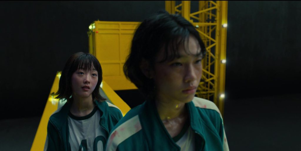 Two Squid Game players in conversation under emotional stress, learning English through movies.