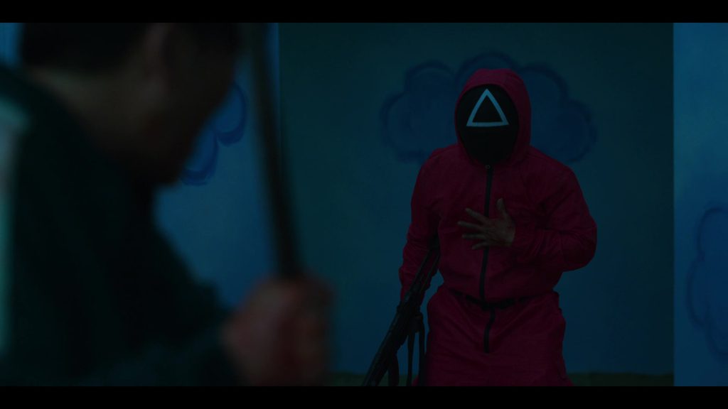 Squid Game guard in a pink suit with triangle mask during a tense confrontation scene.