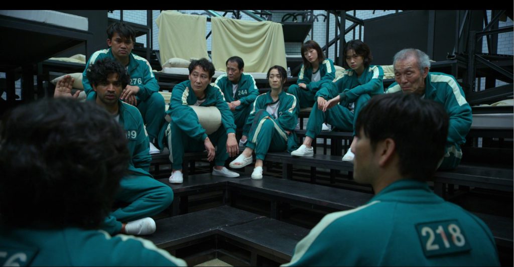 Scene from Squid Game where players sit and discuss strategy, ideal for learning English vocabulary through movies.