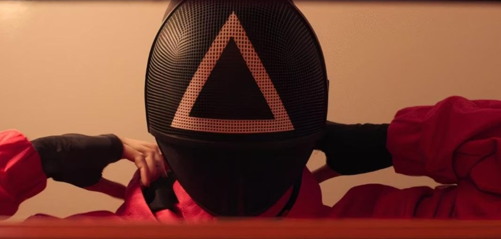 Film Vocabulary Builder for Squid Game S02E02 – Movie for Language A close-up of a masked guard adjusting the iconic triangle mask from Squid Game S02E02. Learn new words with our Film Vocabulary Builder.