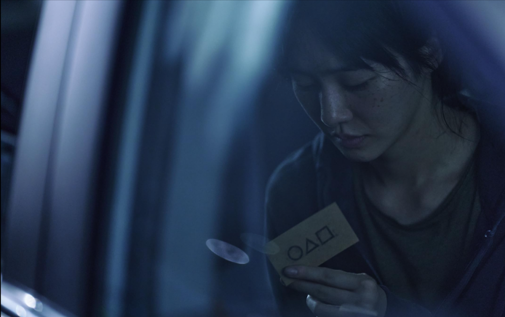 Squid Game Invitation Scene for Film Vocabulary Builder – Language Learning with Netflix Kang No-eul holding a game invitation card from Squid Game S02E02. Build your vocabulary with this iconic moment using our Film Vocabulary Builder.