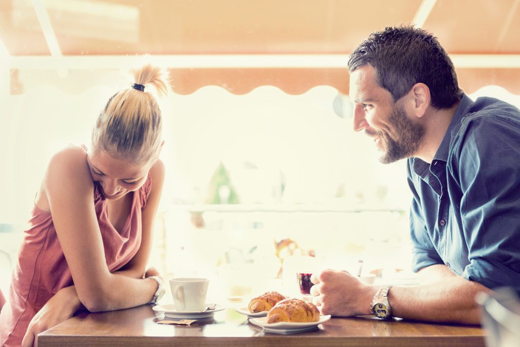 A smiling couple having a conversation over coffee and pastries at a cafe.