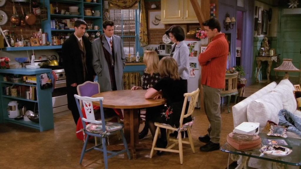 Friends group gathered around the table in Monica’s apartment, Learn Language Cinema moment