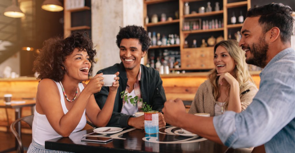 A group of diverse people laughing and enjoying coffee together in a café, symbolizing American English and cultural diversity.