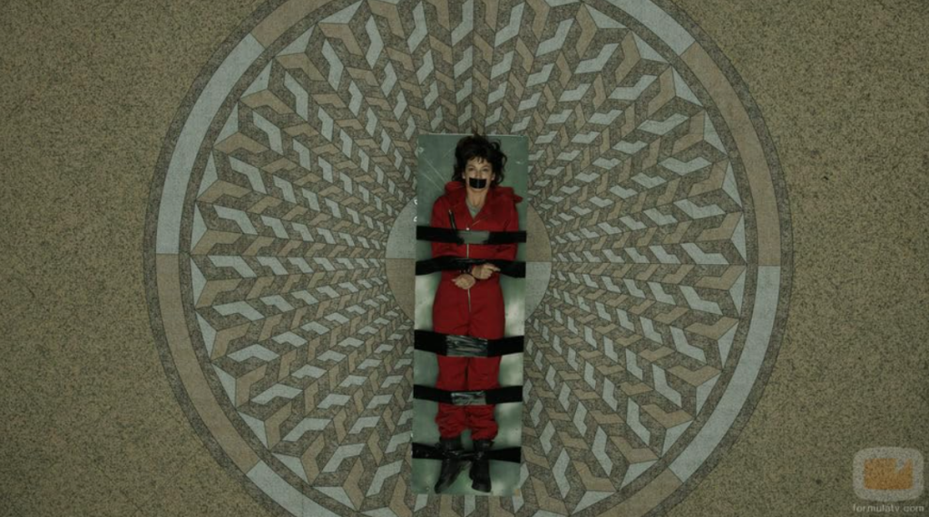 A scene from Money Heist featuring a hostage tied up on a patterned floor.