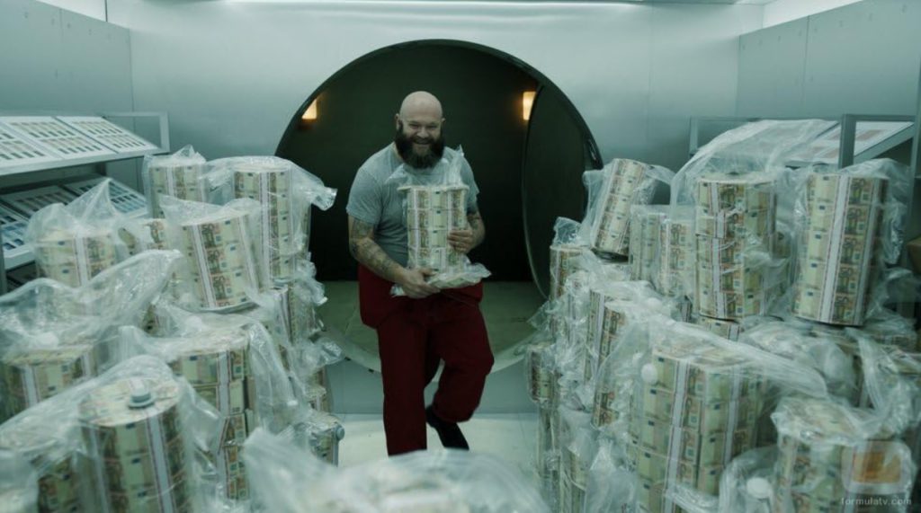 A scene from Money Heist showing a character carrying printed money in a vault.