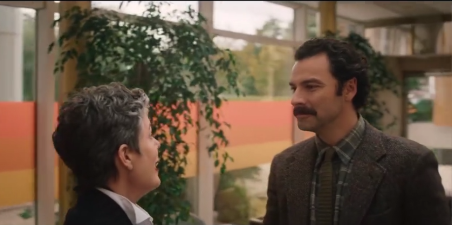 Two characters engaged in a conversation in an office setting, scene from Rival E05.